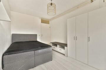 A simple and modern bedroom featuring a gray bed, light-colored flooring, and minimal decor. The room emphasizes functionality and cleanliness.