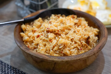 A wooden bowl of freshly cooked fried rice with visible vegetables and protein, accompanied by a spoon on its edge.