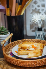 Delicious golden spring rolls displayed in a wicker basket on a plate, filled with fresh vegetables, ideal for culinary presentations, food blogs, menus, and showcasing appetizing cooked treats.