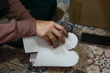 A hand holding an elegant white doorgift box with gold accents, partially opened to reveal its...