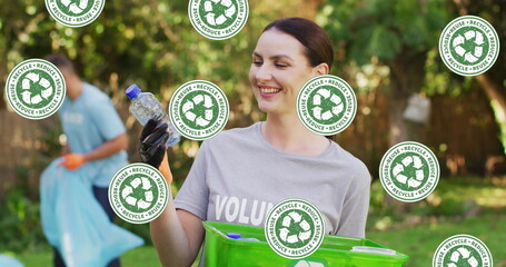 Image of falling recycling icons over happy caucasian woman picking up rubbish in countryside