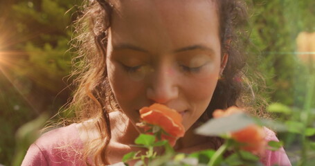 Image of light spots over biracial woman smelling flowers in garden