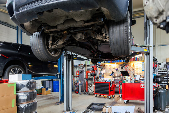 Scenic bottom POV disassembled SUV car with removed gearbox raised on lift elevator at workshop service maintenance station center. Vehicle check-up and repair. Underbody chassis and suspension parts