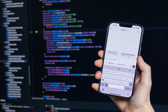 Poznan, Poland &ndash; April 14, 2025: Developer using ChatGPT 4.5 on smartphone while working with code editor on large computer screen