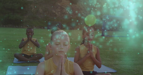 Image of light spots over diverse children practicing yoga and meditating
