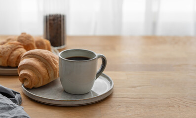 Cup of freshly brewed coffee and croissants on a plate on a wooden table