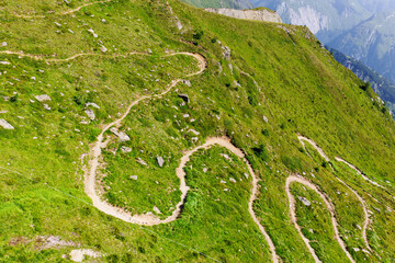 Scenic aerial panoramic view curvy winding serpentine dirt path road alpine mountain peak with...