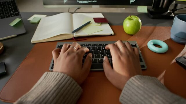 POV shot of unrecognizable software engineer typing on keyboard while working with program code on laptop and PC sitting at office desk