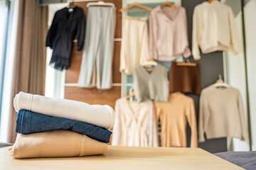 Stacked pile of clothing prepared for resale, donation, or recycling, with wardrobe with outfits in...