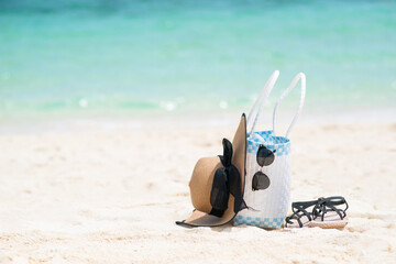 The object of Slippers, Straw Hat, and a bag on the cotton or accessories of the sea travel on a sandy beach with the sea background. holiday summer relaxing and travel concept. Copy space for text.
