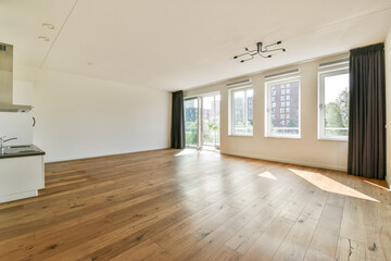 A spacious, modern interior featuring large windows that fill the room with natural light, showcasing a warm wooden floor and minimalist design elements.
