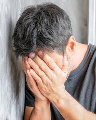 Fototapeta premium Emotional Stress Awareness Portrait of a Man Hiding Face with Hands Against Wall in Realistic Setting