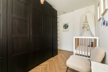 A stylish, modern nursery featuring a wooden crib, cozy armchair, and beautifully designed storage. The room is bright and welcoming with elegant decor.