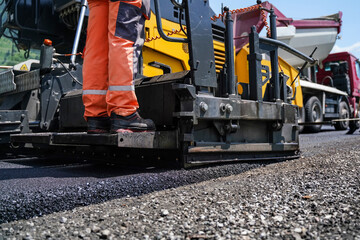 Low angle close-up of asphalt paver machine laying fresh layer of asphalt on road construction...