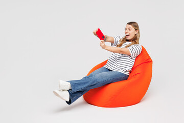Full body young woman wear striped t-shirt casual clothes sit in bag chair use play racing app on mobile cell phone hold gadget smartphone for pc video games isolated on plain solid white background. © ViDi Studio
