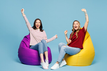 Full body young couple two friends women wearing red casual clothes together sit in bag chair do...