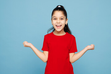 Little kid girl 8-9 years old wears red t-shirt have fun doing winner gesture clench fists say yes isolated on blue color background child studio portrait. Mother's Day love family lifestyle concept.