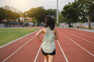 Obraz premium southeast Asian woman runner jogs on red track in outdoor stadium, embracing healthy lifestyle with motivation and wellness as she faces challenge of fitness