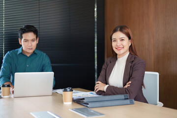 Professional Collaboration and Teamwork. A confident businesswoman smiling in a meeting while her colleague works on a laptop.