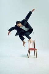 Elegant man leaping off vintage chair in raw expression of freedom and corporate rebellion against...