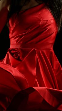 Stunning Black-Haired Woman in Ruby Red Dress and High Heels Gracefully Posing Against a Black Background, Captured in Super Slow Motion. Camera Rotation. Speed Ramp Effect. Vertical Aspect Ratio.