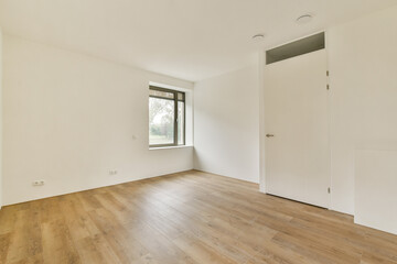 A spacious and modern interior room with wooden flooring and a large window, featuring minimalist decor and a focus on natural light.