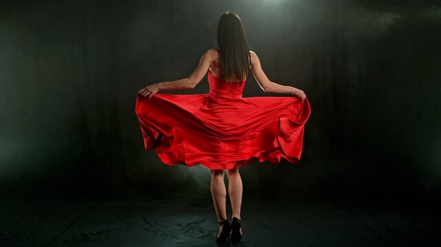 Stunning Black-Haired Woman in Ruby Red Dress and High Heels Gracefully Posing Against a Black Background, Captured in Super Slow Motion for a Dramatic and Elegant Fashion Cinematic Effect.