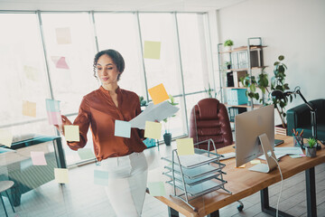 Confident businesswoman organizing tasks in a bright, modern office with notes on glass, demonstrating productivity