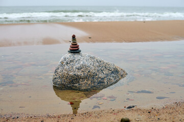 Smooth stones meticulously stacked on large rock by serene beach. Overcast sky creates calm...