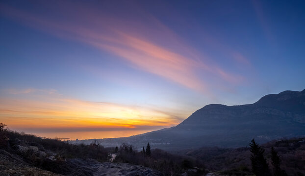 Vibrant sunset over coastal mountains with dramatic clouds in a serene landscape