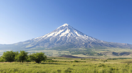 Fototapeta premium Majestic snow capped mountain peak under clear blue sky, surrounded by green fields and trees