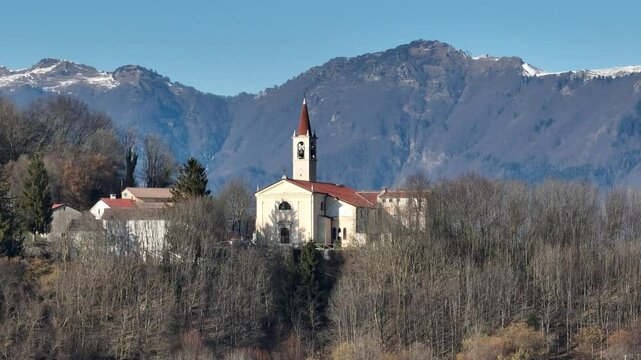Aerial telephoto shot with smooth right-to-left tracking, capturing the Church of Bolca among Verona&rsquo;s hills, with Monte Carega rising imposingly in the background