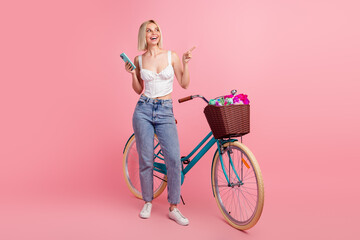 Charming young woman with a bike posing against a pink backdrop exuding happiness and trendy summer...