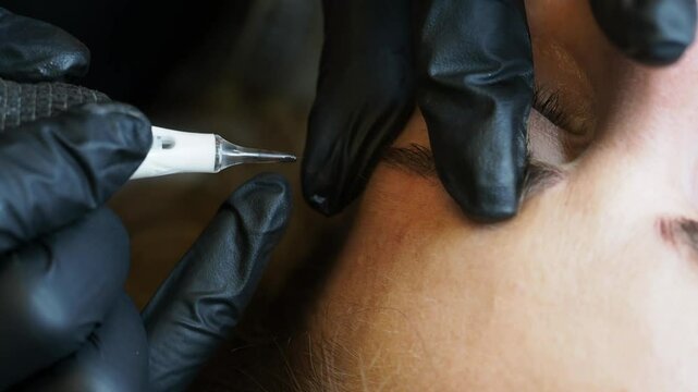 Esthetician applies microblading with blue tool on client eyebrow , slow motion frontal close-up