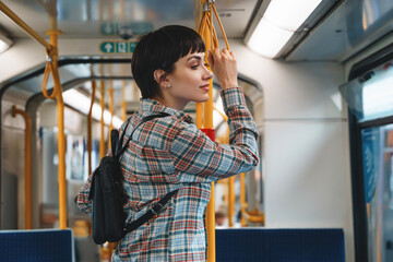 Young woman enjoying a quiet ride on a public transit train while holding onto a pole in an urban...