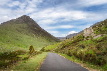 A tranquil road winds gracefully through vibrant green hills in Silent Valley leading towards majestic Mourn Mountains that rise under soft cloudy sky filled with serenity and beauty, Northern Ireland