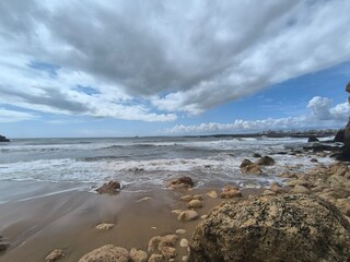 Golden light reflects on water as waves hit the rocky shore. 