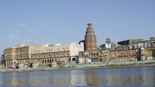 The view of Keshi Ghat at the Yamuna River in Vrindavan captures several temples and people walking on the sides, with reflections in the water adding beauty to the scene.