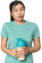 Chinese athlete with protein shake shrugs shoulders and open eyes confused.