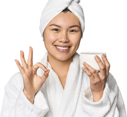 Chinese woman with moisturizer in robe cheerful and confident showing ok gesture.