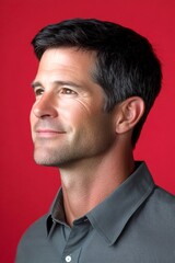 Obraz premium Red solid background. A modern and graceful man smiling naturally. Artwork art of style for aging men. Classy men's shoulder-length taper haircut - midlife white man with black hair.
