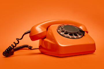 Bold orange rotary phone on vibrant matching backdrop. Concept of vintage aesthetic, retro...