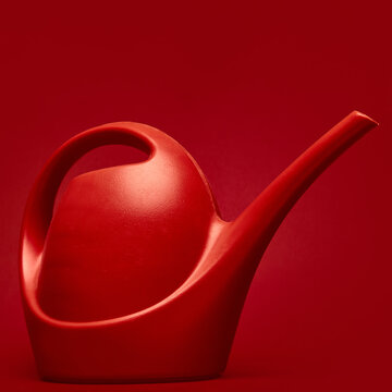 Vibrant red plastic watering can stands against monochromatic deep red background. Gardening supplies, cultivation, care, growth, eco ads, gardening blogs, product posters.