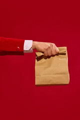 Hand holding kraft paper bag against bold red background. Express delivery with eco-friendly...