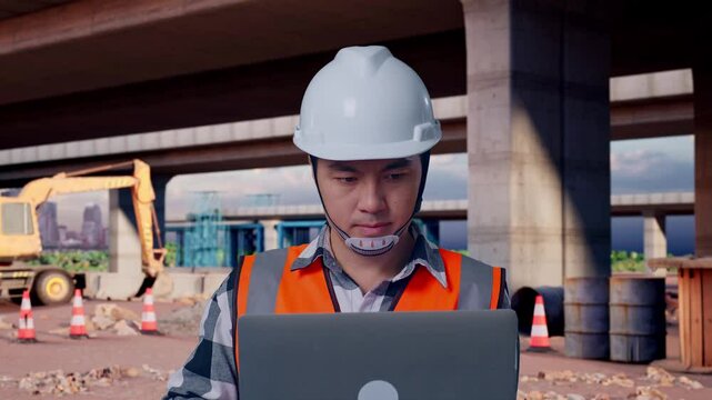 Close Up Of Asian Male Engineer With Safety Helmet Working On A Laptop While Standing At The Site of Highway Construction