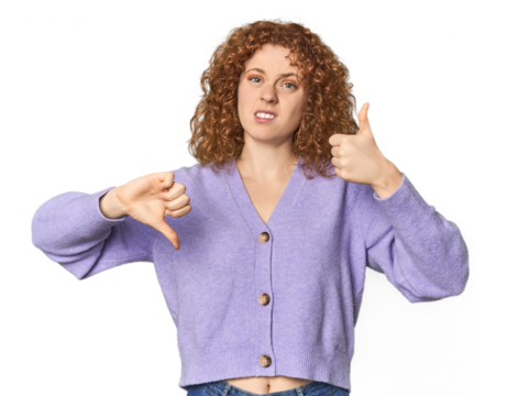 Young Caucasian redhead woman showing thumbs up and thumbs down, difficult choose concept
