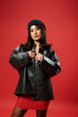 Young woman in stylish attire showcases modern fashion against a bold red backdrop