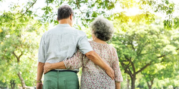 Elderly Asian couple walking in park. Elderly Asian couple enjoy nature in park. Elderly couple, senior man and woman in green park, walk and hug each other. Elderly couple enjoy outdoors park