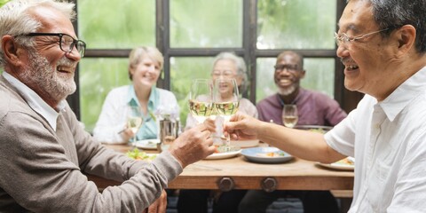 Group of diverse seniors enjoying a meal together, smiling and toasting. Elderly friends, happy gathering, cheerful seniors, diverse group, joyful meal. Senior friends celebrating with wine for lunch.