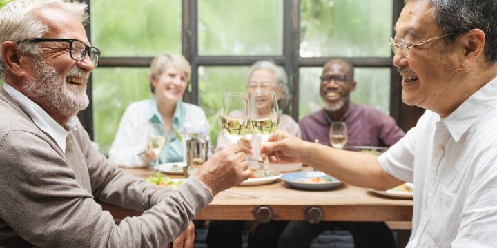 Group of diverse seniors enjoying a meal together, smiling and toasting. Elderly friends, happy gathering, cheerful seniors, diverse group, joyful meal. Senior friends celebrating with wine for lunch.